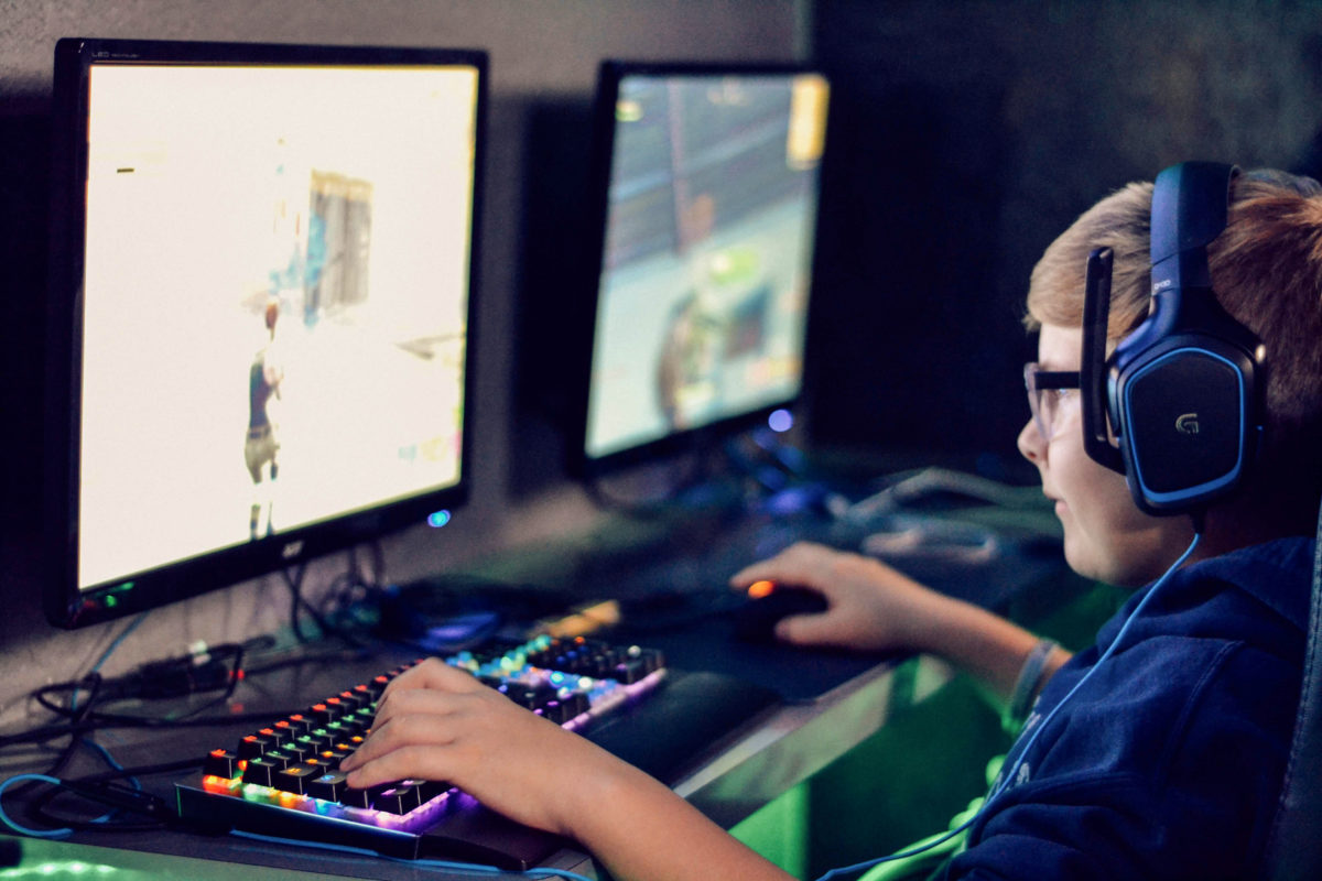 Jugendlicher mit Kopfhörern vertieft in Computerspiel vor zwei großen PC-Bildschirmen