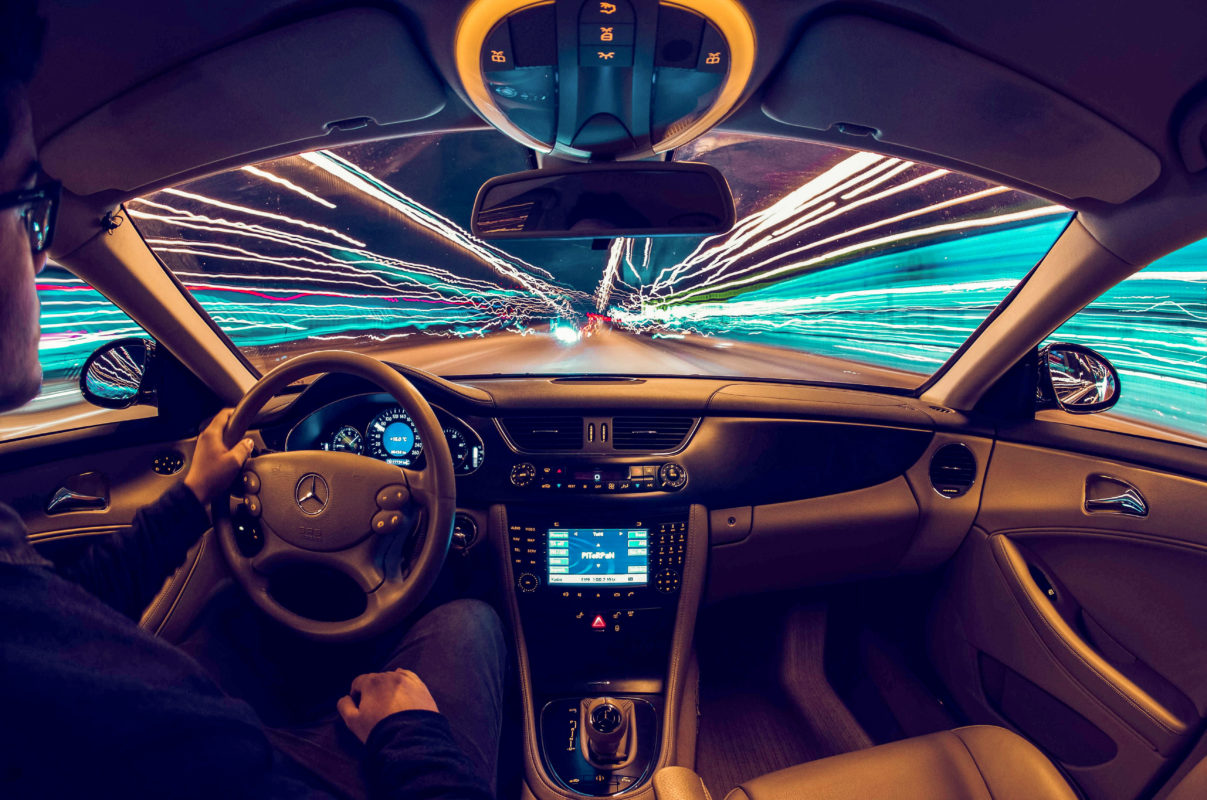 Fahrzeug Innenaufnahme: Mann fährt mit hohem Tempo vom Unfallort weg. In den Scheiben sieht man lediglich Lichter, die aufgrund der Geschwindigkeit bereits als Streifen zu sehen sind. 