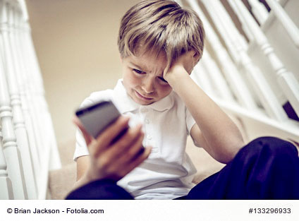 cyber mobbing - Kind schaut traurig aufs Smartphone