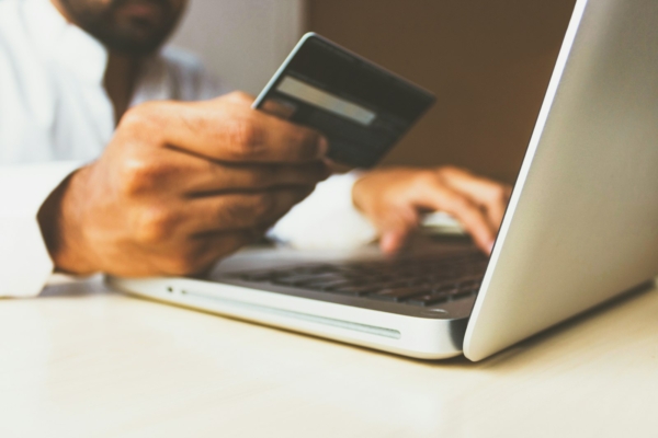 Person mit Bankkarte in der Hand bestellt am Laptop in einem Online-Shop